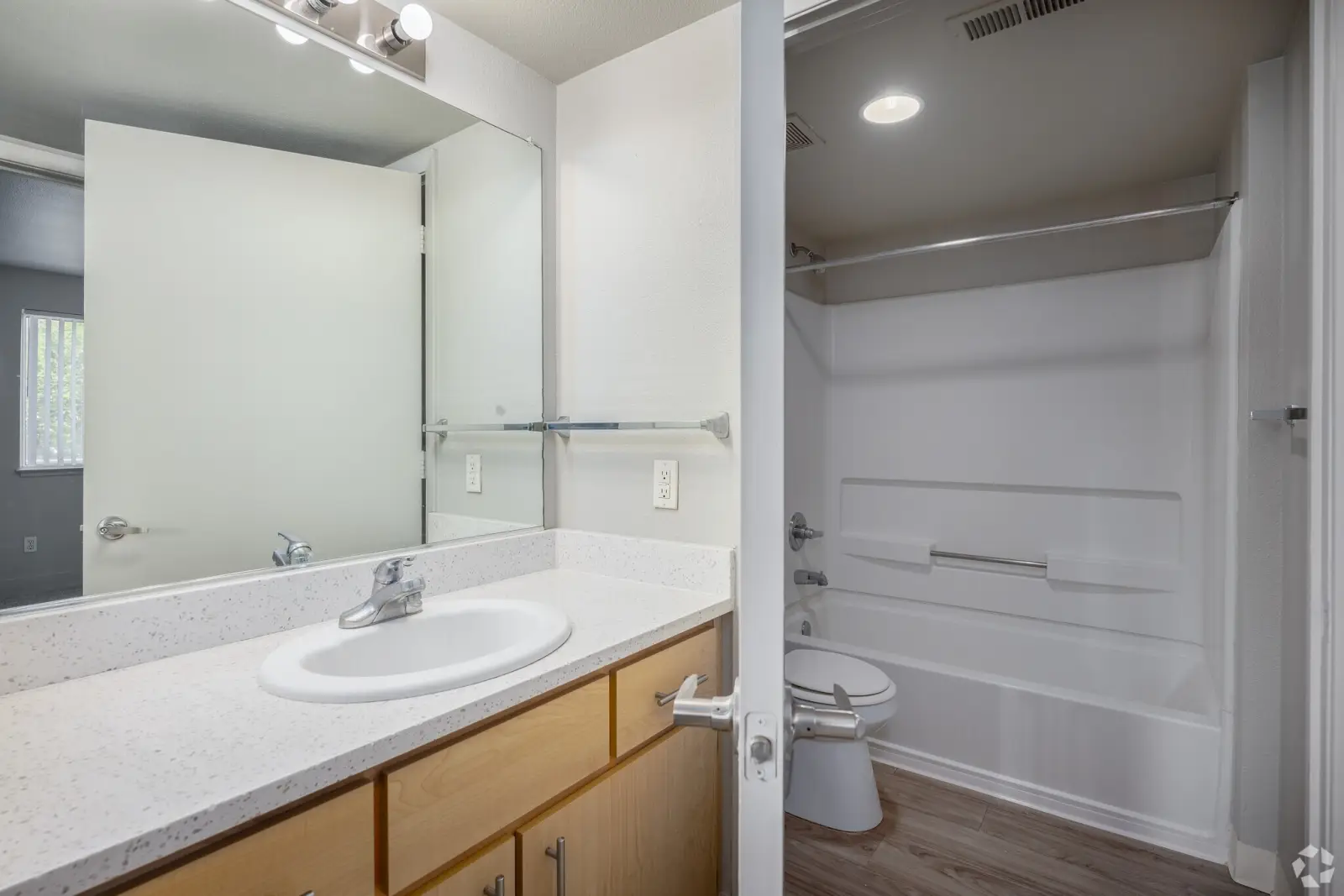 Apartment bathroom with single sink vanity, large mirror, and bathtub with shower rod