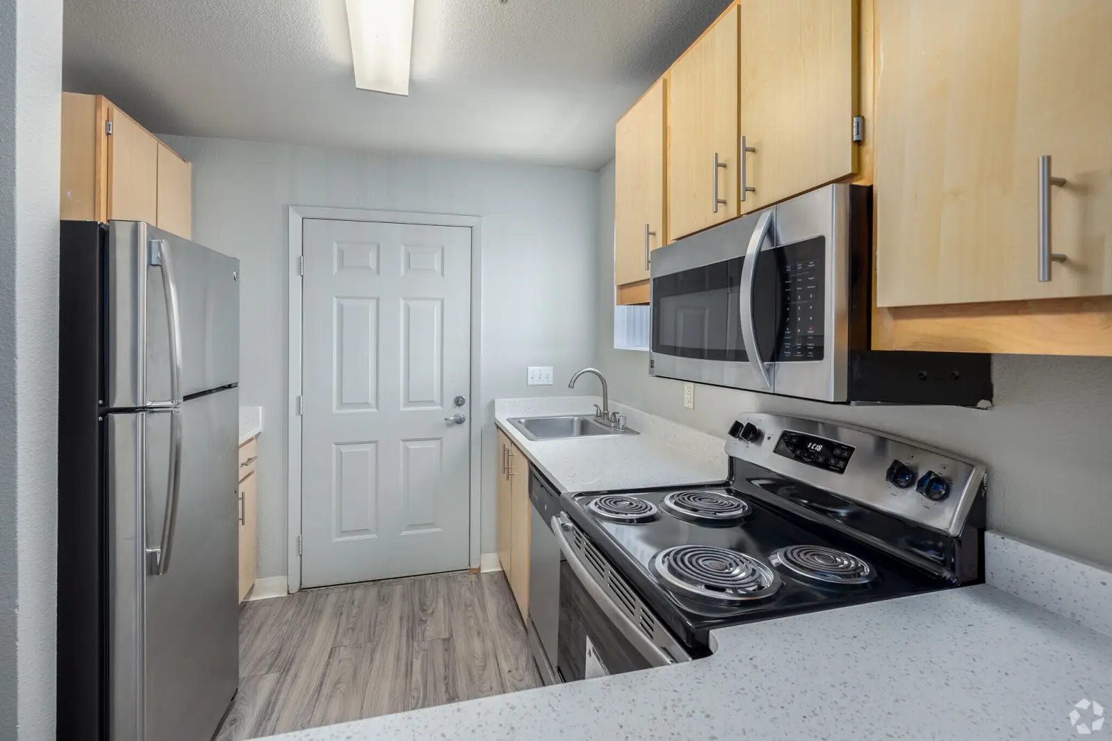 Renovated apartment kitchen with stainless steel fridge, microwave, electric stove and light wood cabinets