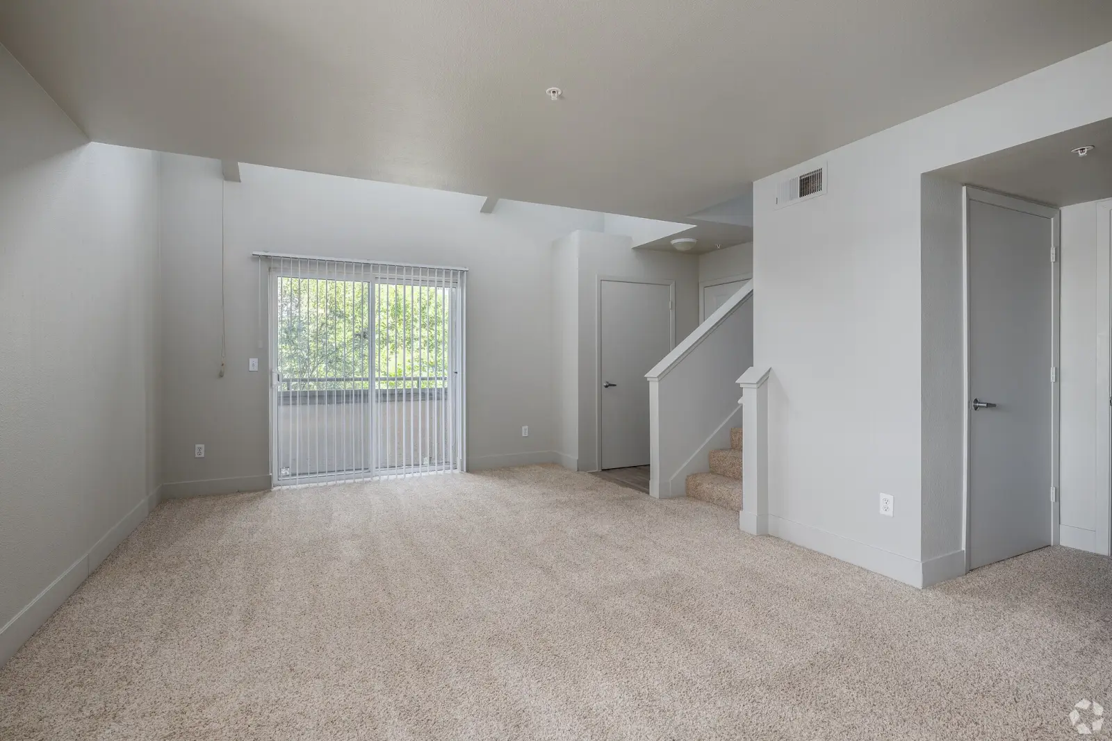 Bright carpeted living room with sliding glass door, balcony view, and interior stairway in a renovated Davis apartment