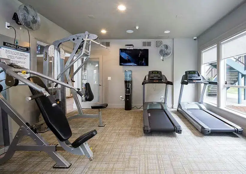 Apartment community fitness center with treadmills, weight machine, TV, and water dispenser