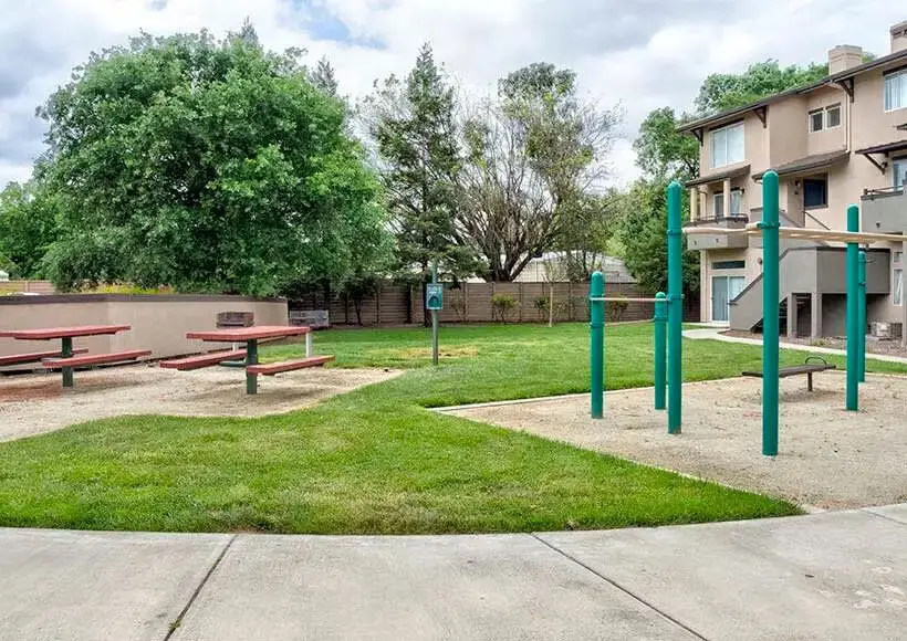 Apartment courtyard with picnic tables, grassy lawn, and outdoor fitness bars beside a three-story renovated building