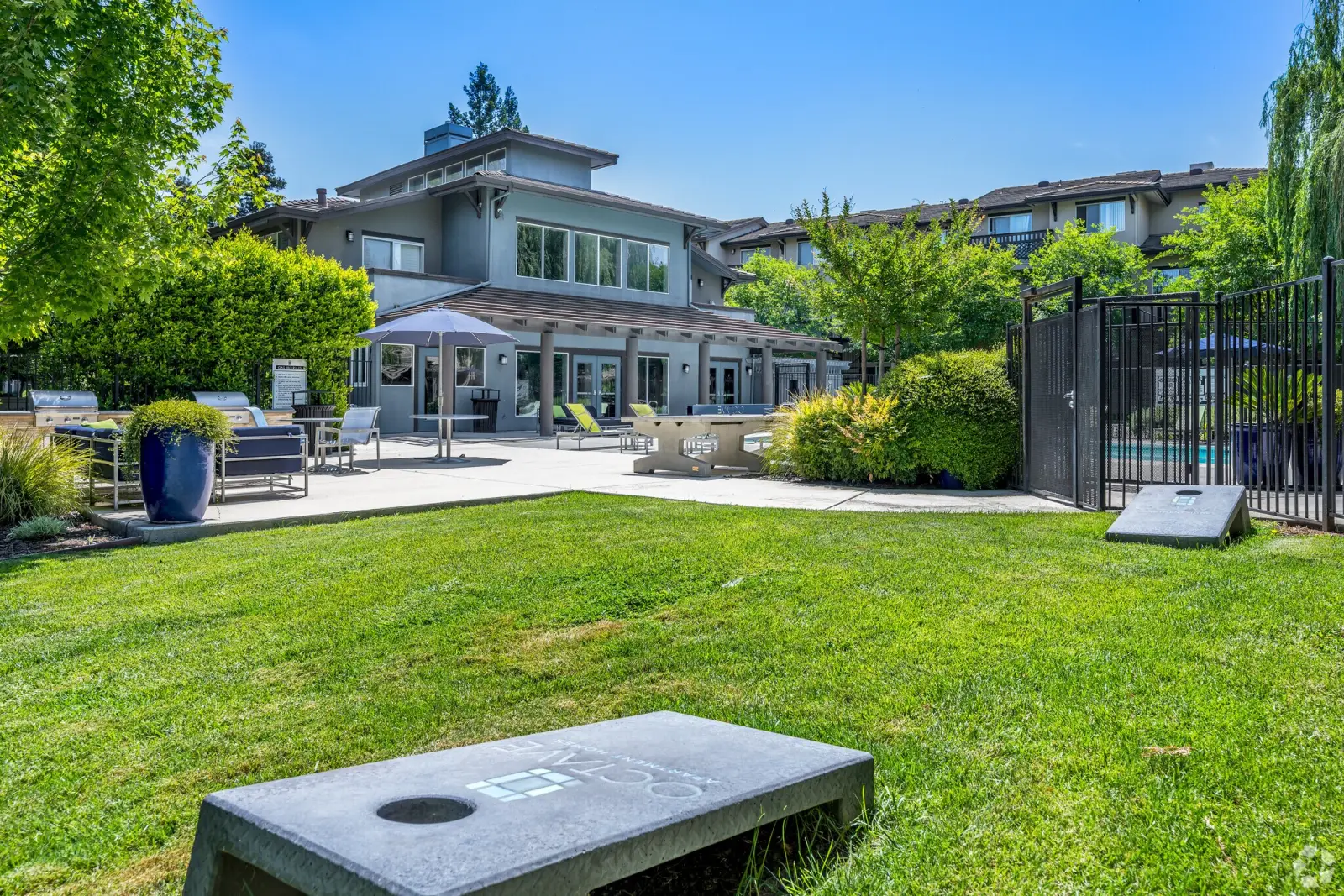 Cornhole boards on a grassy lawn beside the clubhouse and pool at an apartment community in Davis, CA.