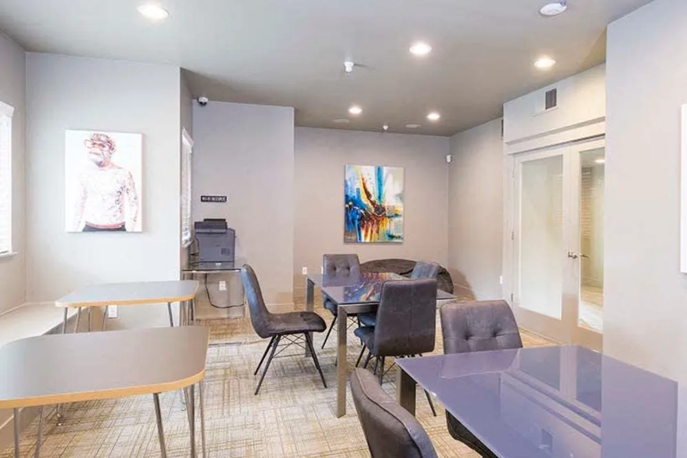 Community study lounge with tables, chairs, printer, and artwork in a renovated student apartment building