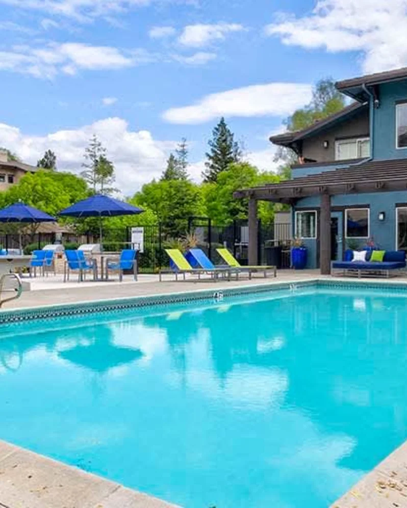 Outdoor apartment community pool with lounge chairs, umbrellas, and building in the background