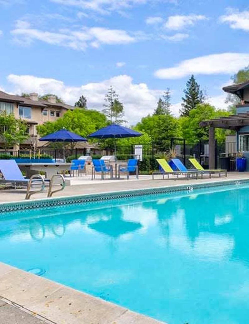 Outdoor swimming pool with lounge chairs and blue umbrellas at a renovated apartment complex in Davis, CA