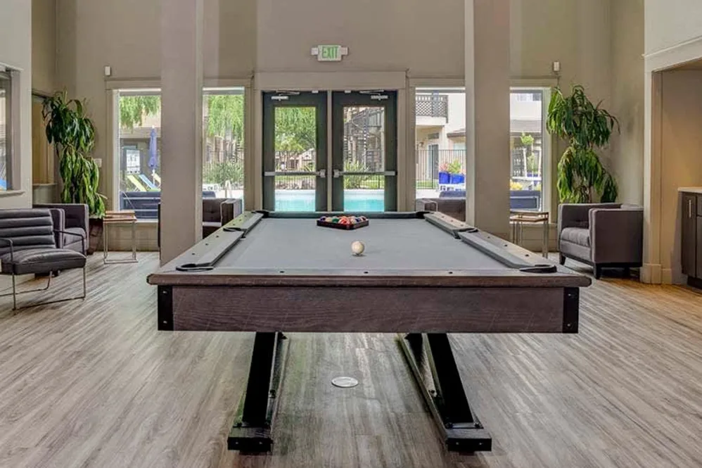 Community game room with pool table, seating, and view of the outdoor pool at student apartments near UC Davis